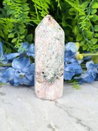 A white, moss-covered stone sits on a marble surface, surrounded by vibrant blue flowers.