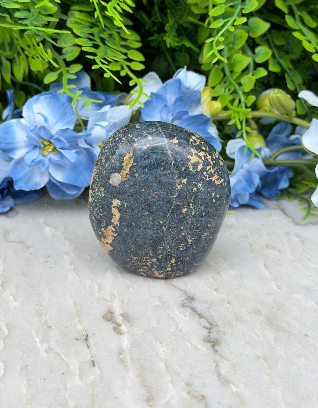 A black rock rests on a white surface, surrounded by vibrant blue flowers.