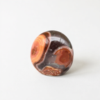 A round, multicolored stone with a unique pattern sits on a white surface.