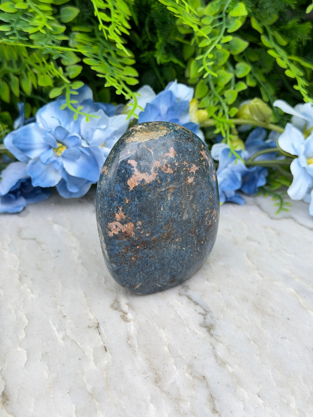 A dark blue rock rests on a white surface, surrounded by vibrant blue flowers.
