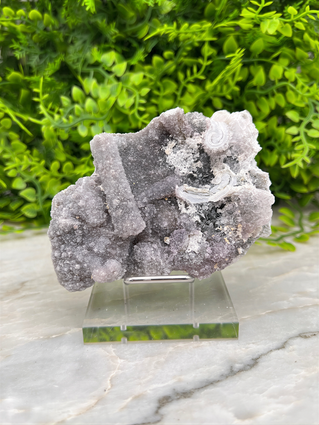 a piece of purple crystal displayed on a clear glass stand, with a blurred green background.