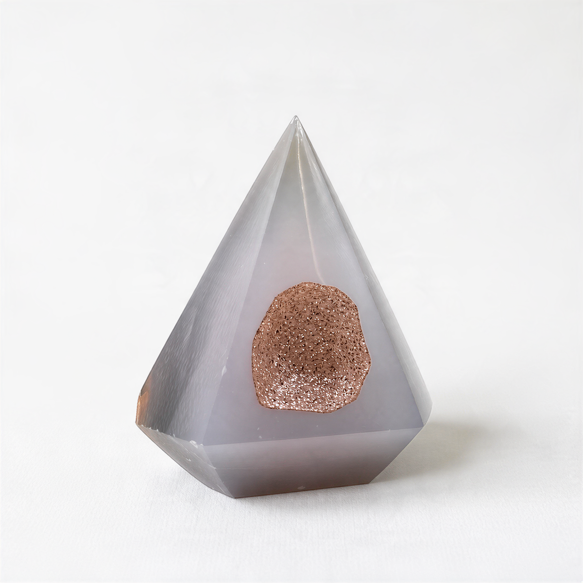 A gray, triangular crystal with a small, round, brownish-colored object in the center.