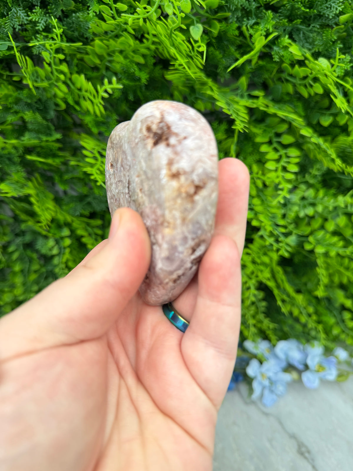 A hand holding a small rock against a backdrop of lush green foliage.