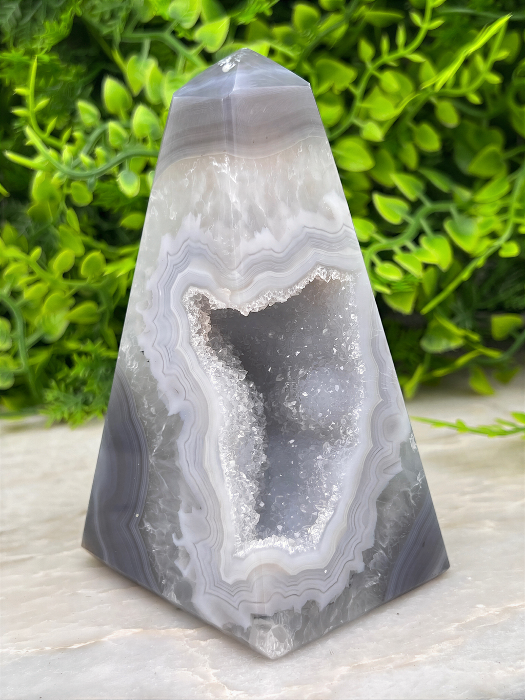 A triangular geode with a large central opening revealing a crystal-like interior, surrounded by a pattern of white and gray minerals.