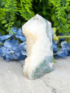 a white and green crystal formation, surrounded by blue flowers, creating a serene and natural setting.