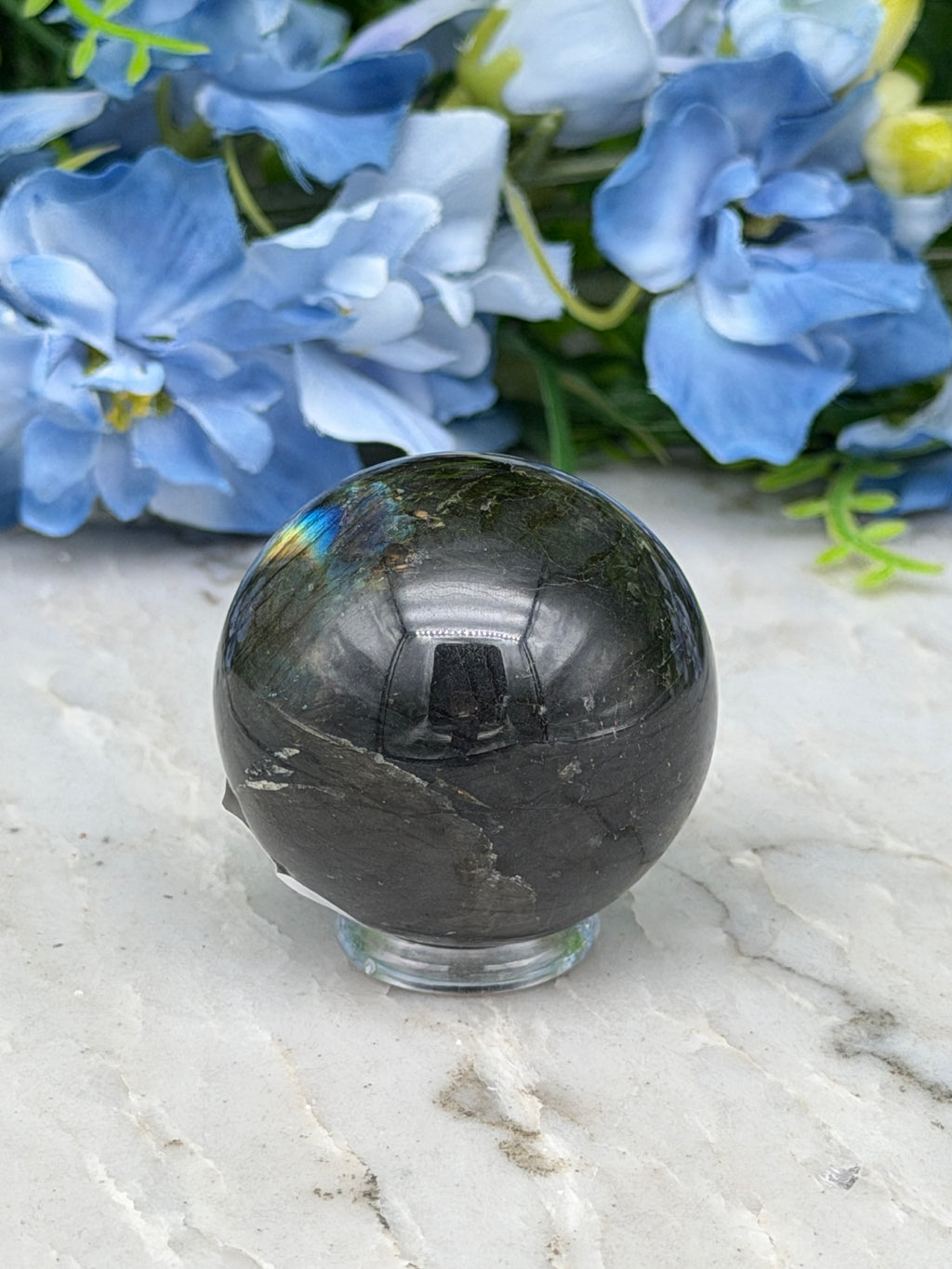 a black crystal ball resting on a white marble surface, with a bouquet of blue flowers in the background.