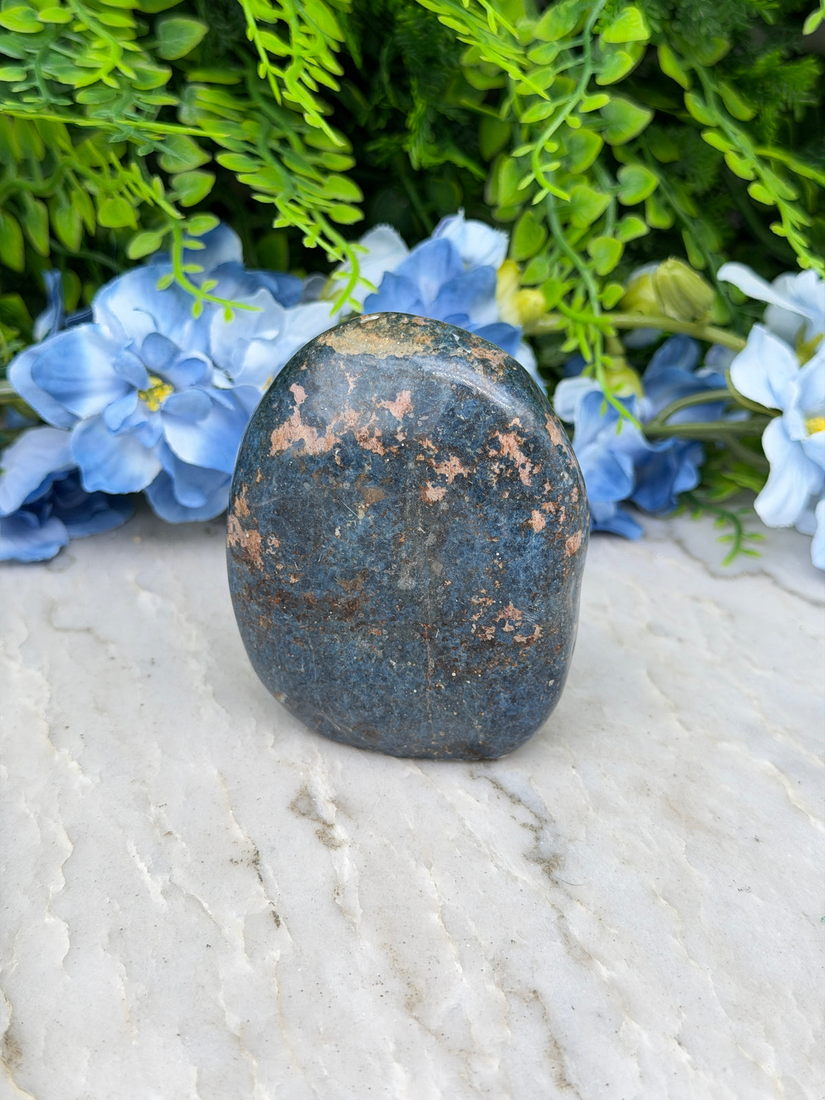 A dark blue rock rests on a white surface, surrounded by vibrant blue flowers.