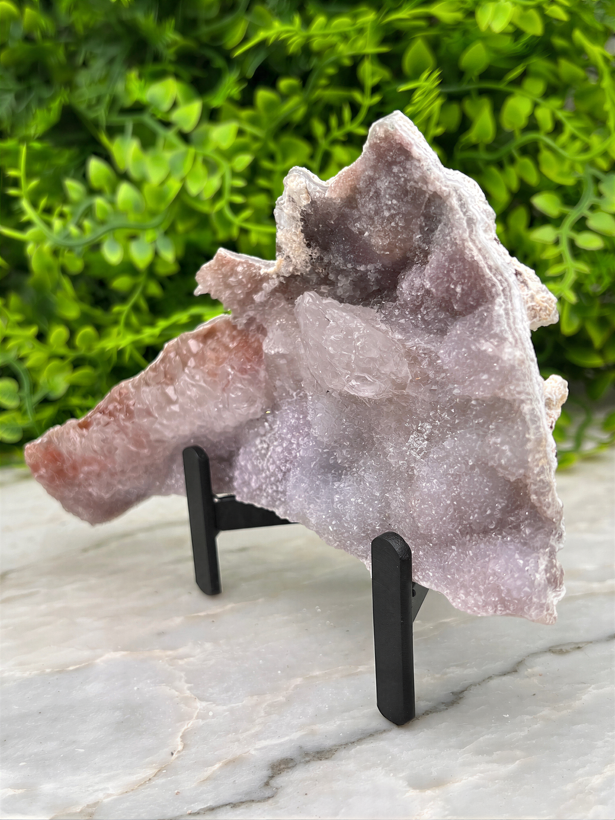 a large piece of amethyst geode placed on a stand, with a blurred green background.