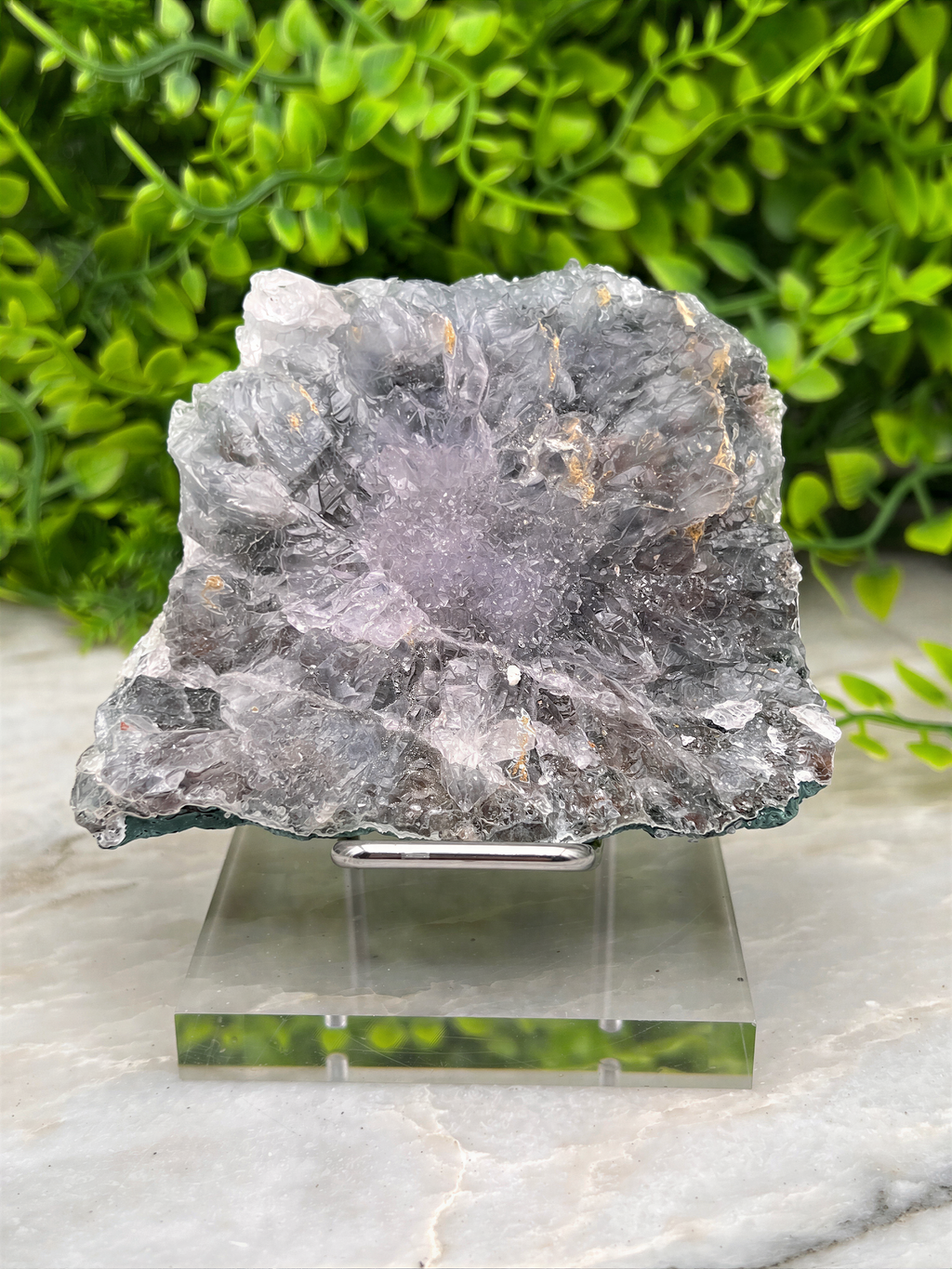 a large, irregularly shaped piece of gray rock with a purple hue, placed on a clear glass stand.