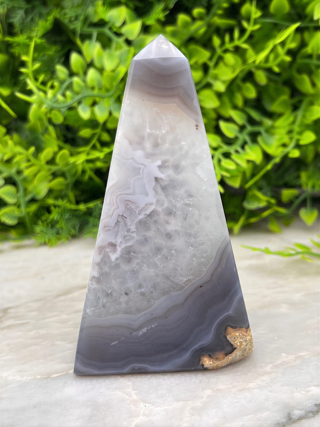 A triangular agate stone with a unique pattern of gray and white bands, set against a blurred green background.