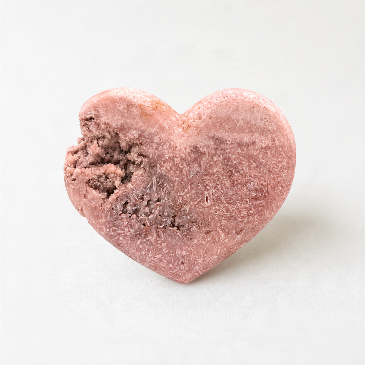 A heart-shaped object made of a pink material, possibly clay or a similar material, with a bite taken out of it.