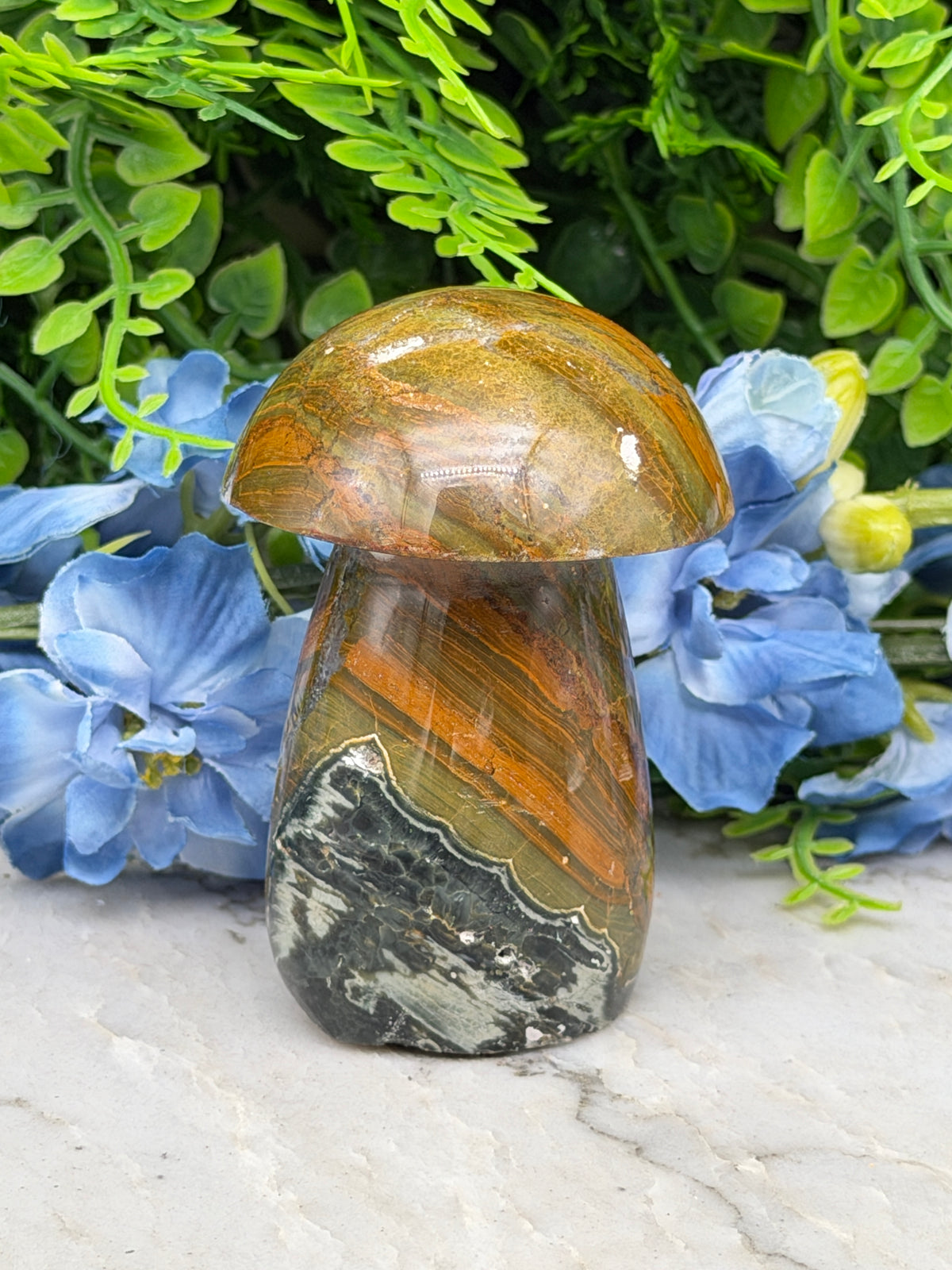 a close-up view of a natural mushroom-shaped rock with a striped pattern, set against a backdrop of blue flowers.