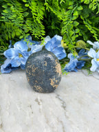 A black rock rests on a white surface, surrounded by vibrant blue flowers.