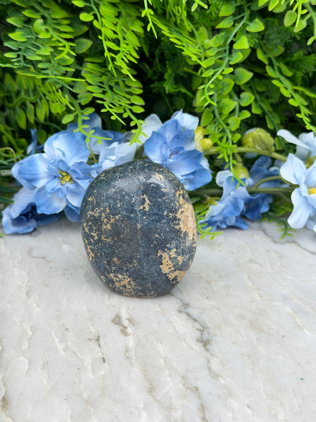 A black rock rests on a white surface, surrounded by vibrant blue flowers.