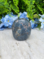 A dark blue rock rests on a white surface, surrounded by vibrant blue flowers.