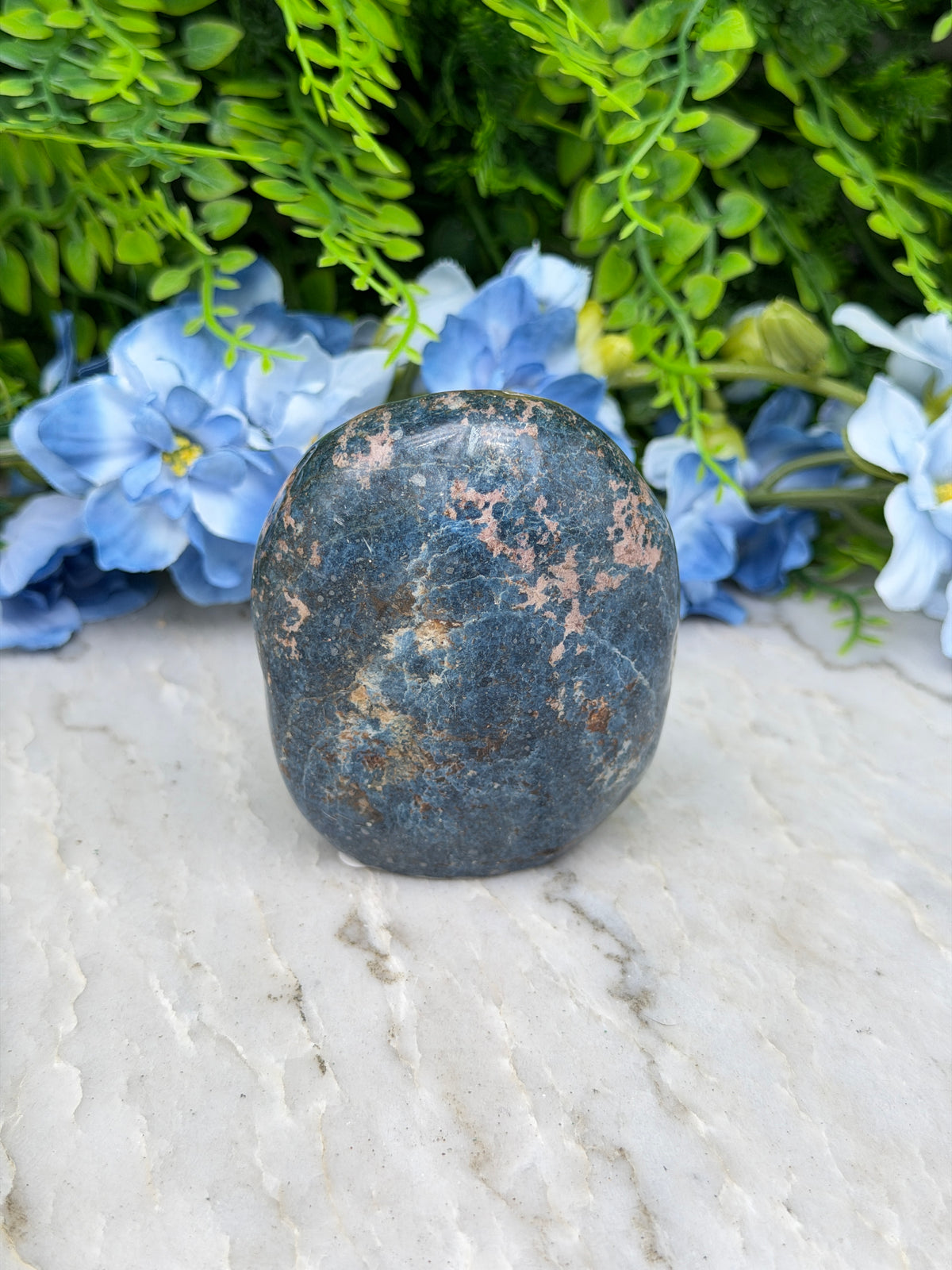 A dark blue rock rests on a white surface, surrounded by vibrant blue flowers.