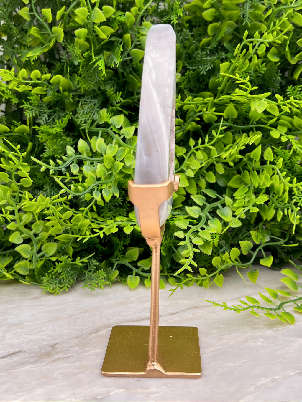 a gold-colored metal stand with a white crystal or gemstone on top, placed on a marble surface.