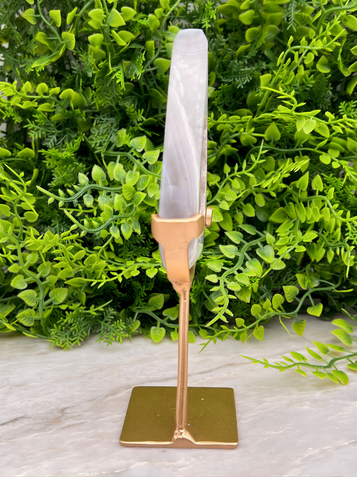 a gold-colored metal stand with a white crystal or gemstone on top, placed on a marble surface.