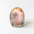 a round, glass-like object with a pink and orange color scheme, sitting on a white surface.