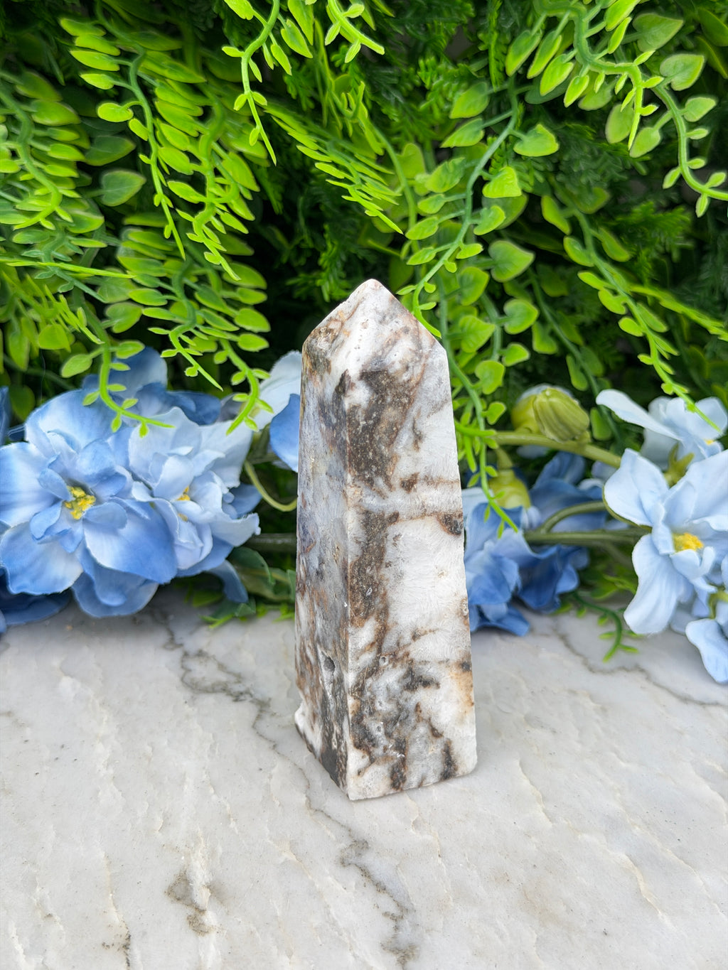 a marble stone surrounded by lush green foliage and blue flowers, creating a serene and natural setting.