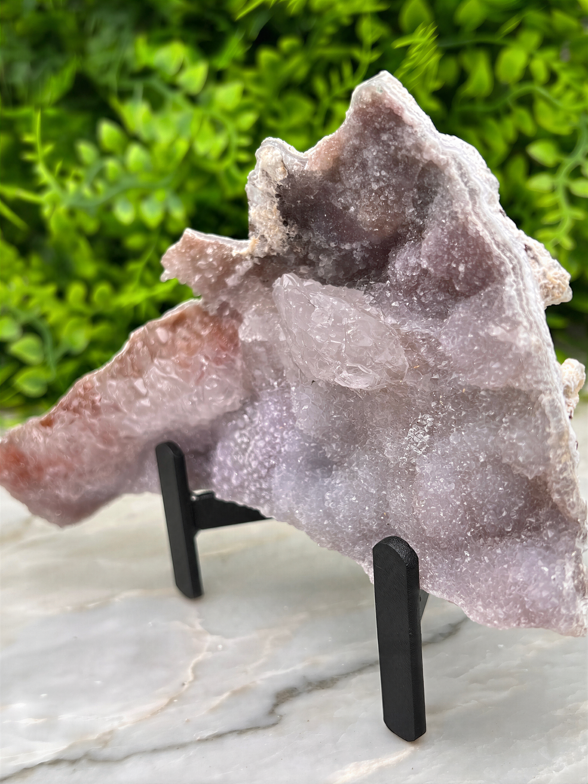a large, irregularly shaped piece of purple rock or gemstone, placed on a stand and surrounded by greenery.