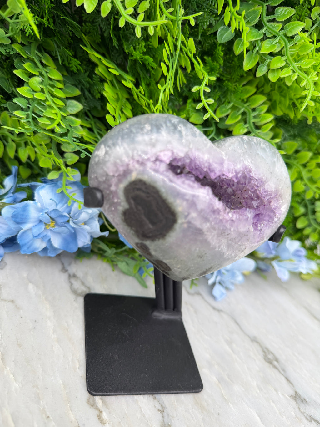 a purple amethyst crystal surrounded by green foliage and blue flowers.