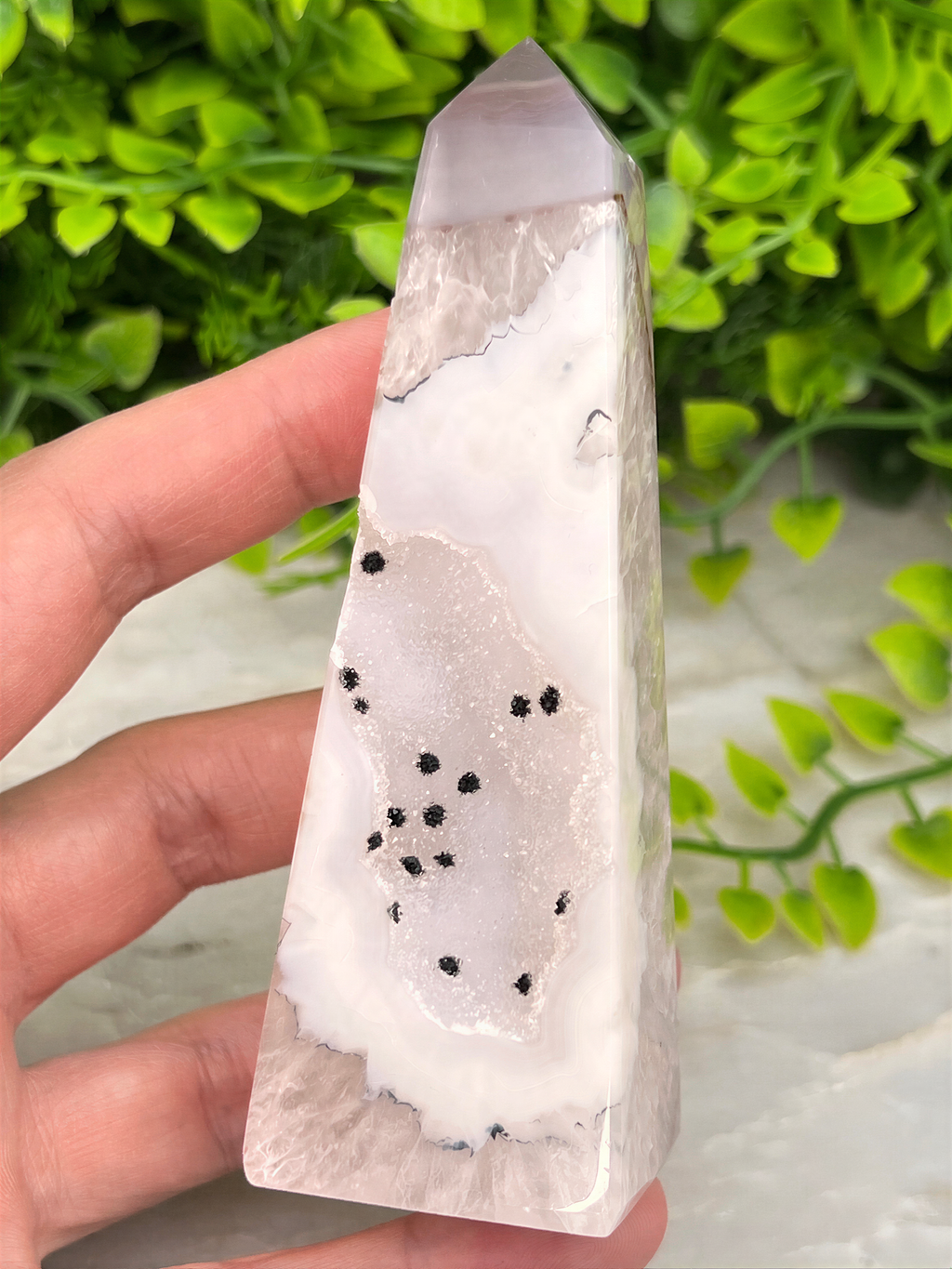 A hand is holding a clear crystal with a unique pattern of black dots on a white background.