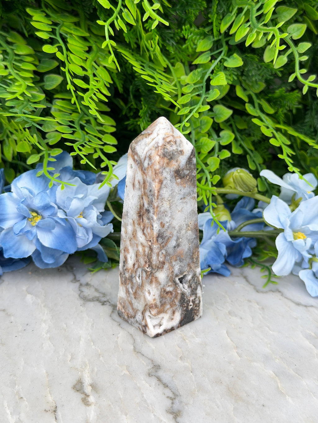 a close-up view of a stone or crystal surrounded by lush green foliage and vibrant blue flowers.