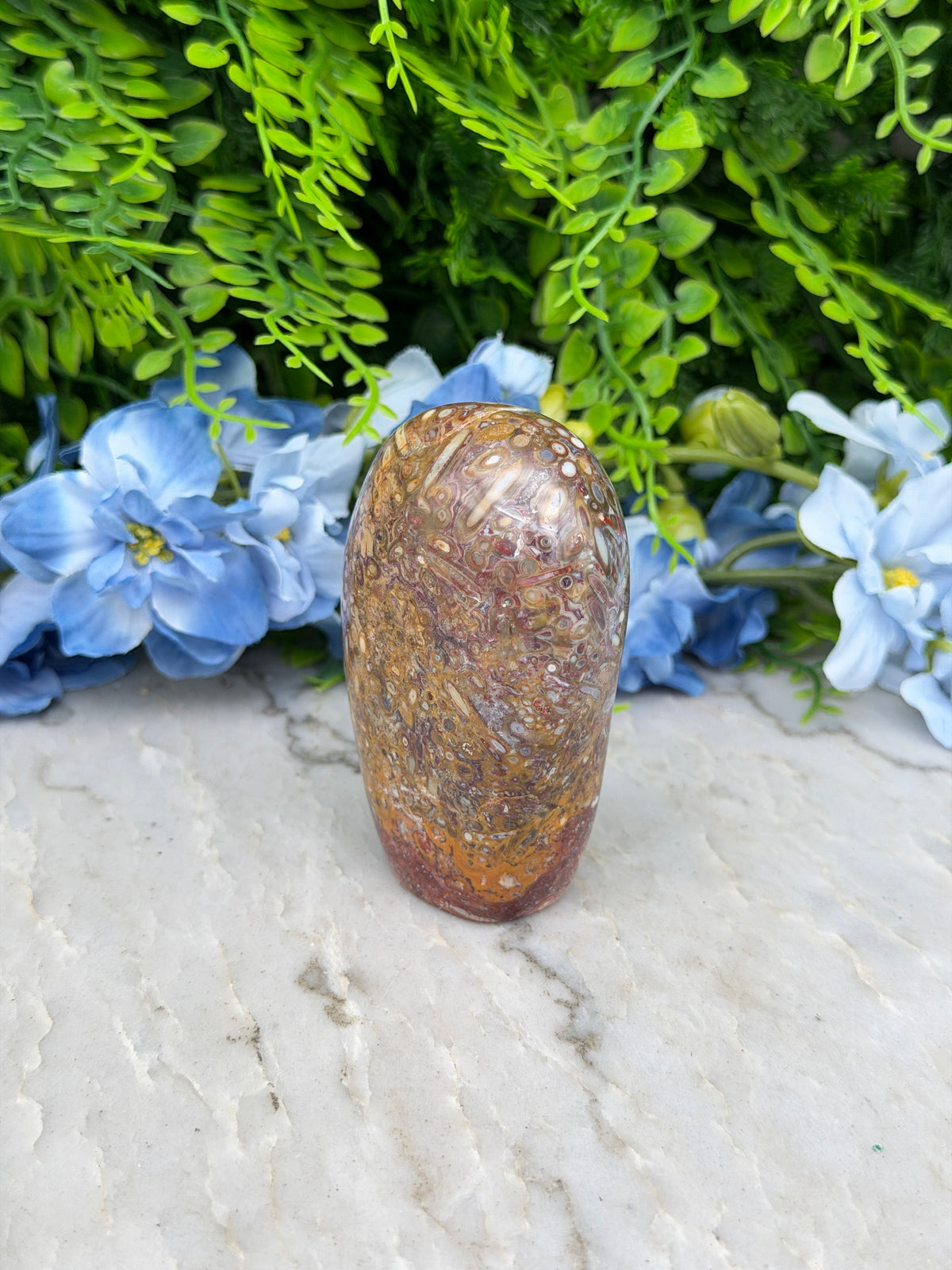a close-up view of a rock or shell resting on a white surface, surrounded by lush green foliage and delicate blue flowers.