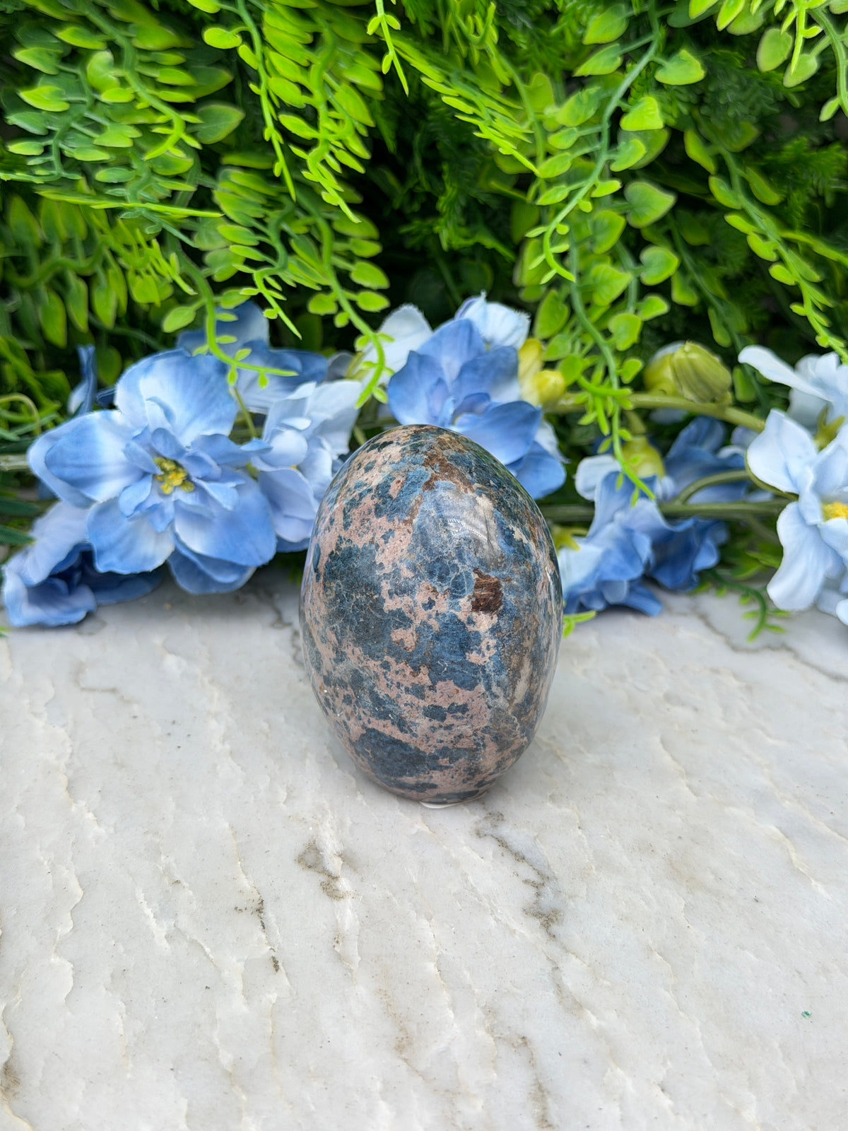 a close-up view of a speckled rock resting on a white surface, surrounded by vibrant blue flowers.
