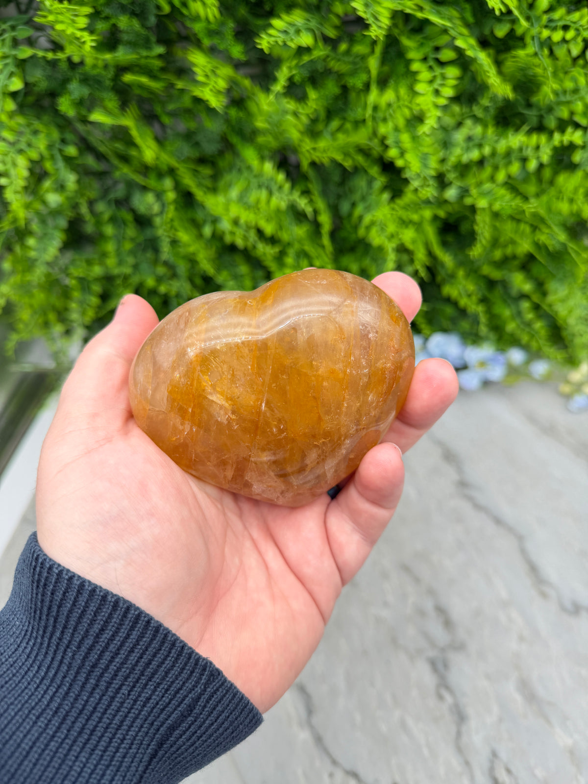 A hand holding a yellowish-brown rock against a backdrop of green foliage.