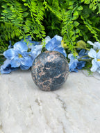 a close-up view of a blue flower and a black and brown rock, with the rock positioned on a white surface.