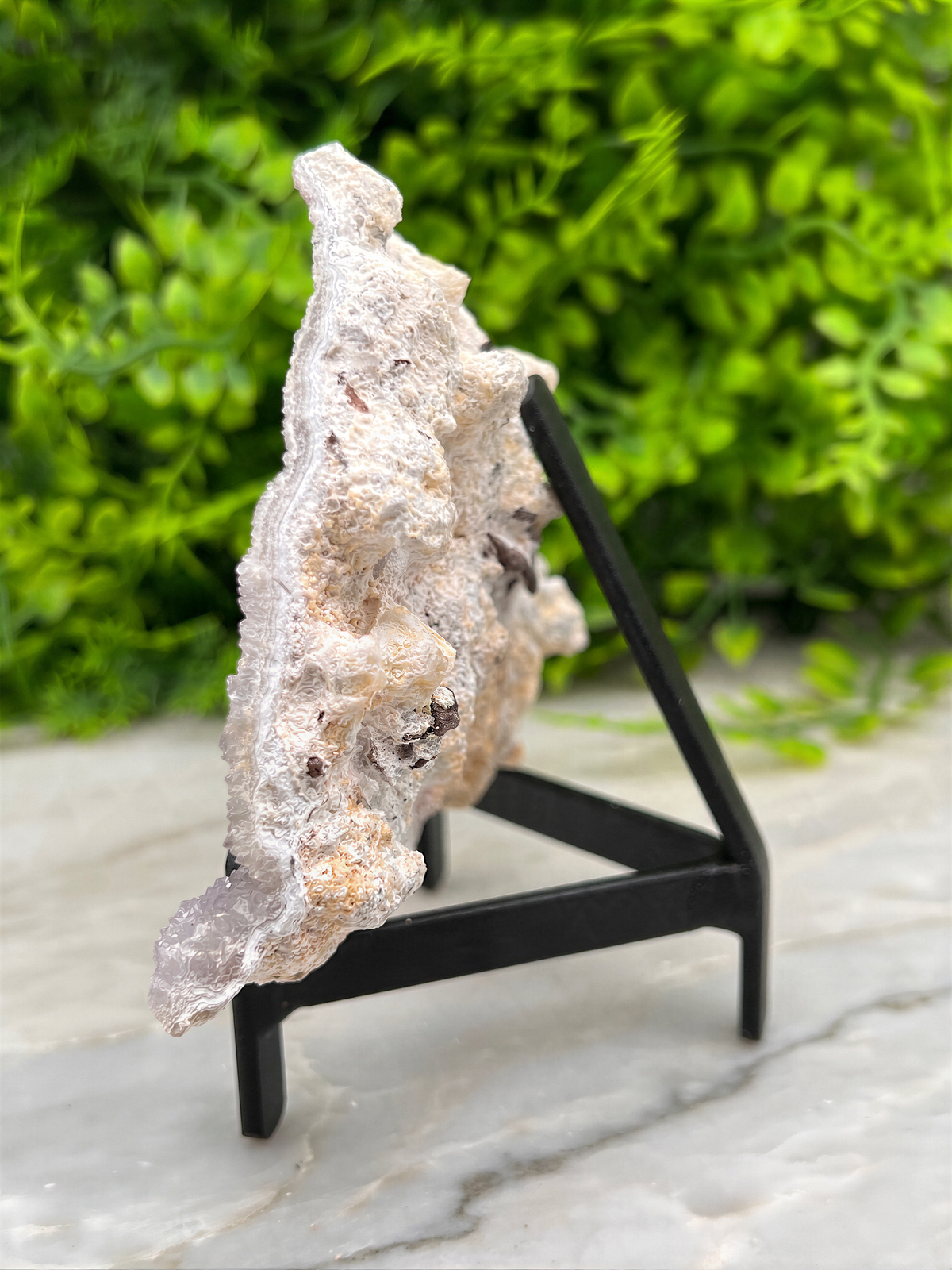 a piece of white rock with a rough, jagged surface, placed on a black stand and set against a blurred green background.
