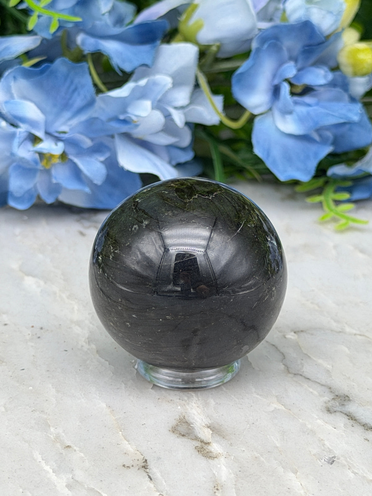 a black crystal ball surrounded by blue flowers, with the flowers appearing to be in full bloom.