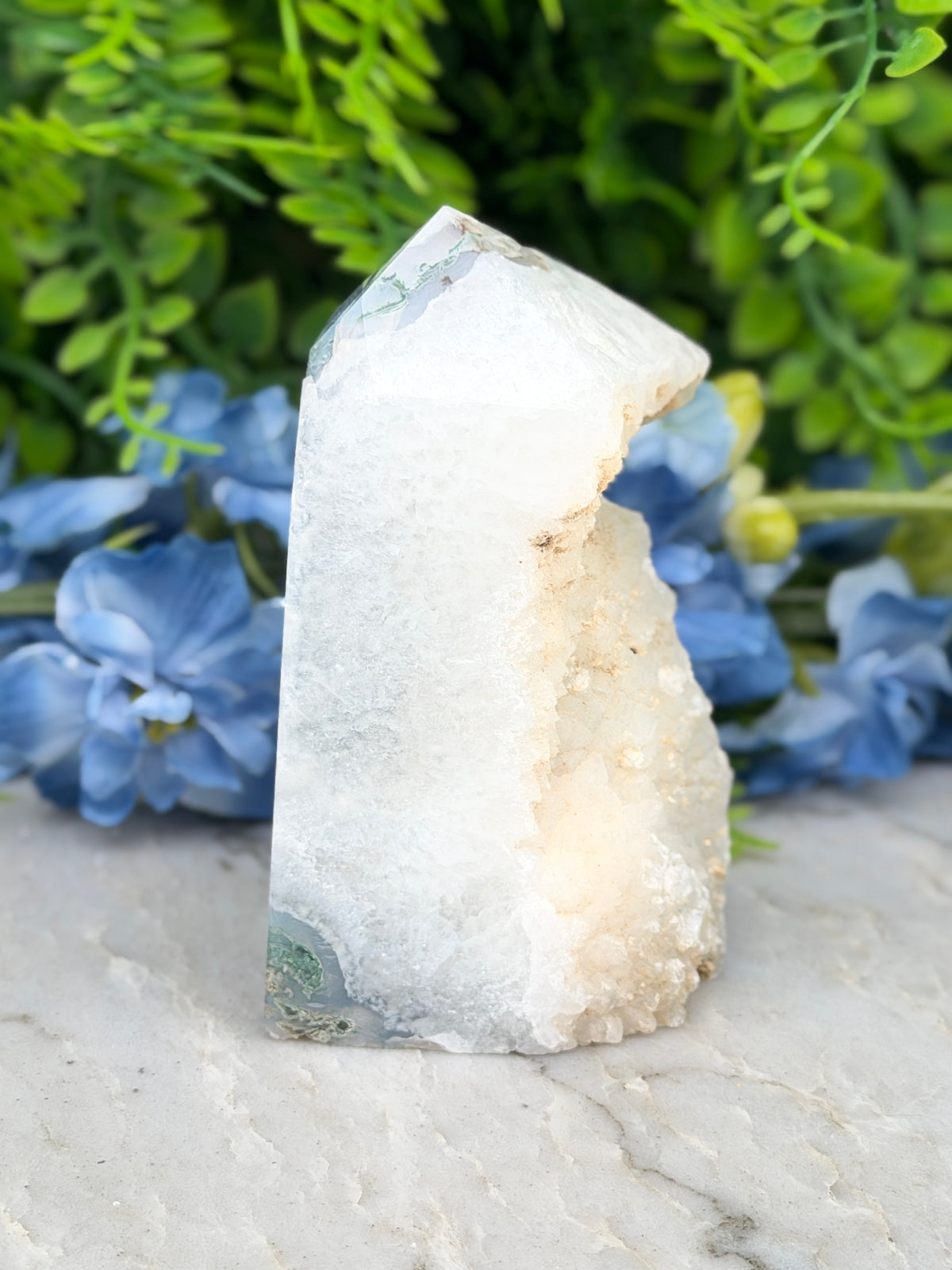 a white crystal with a jagged edge, surrounded by blue flowers.