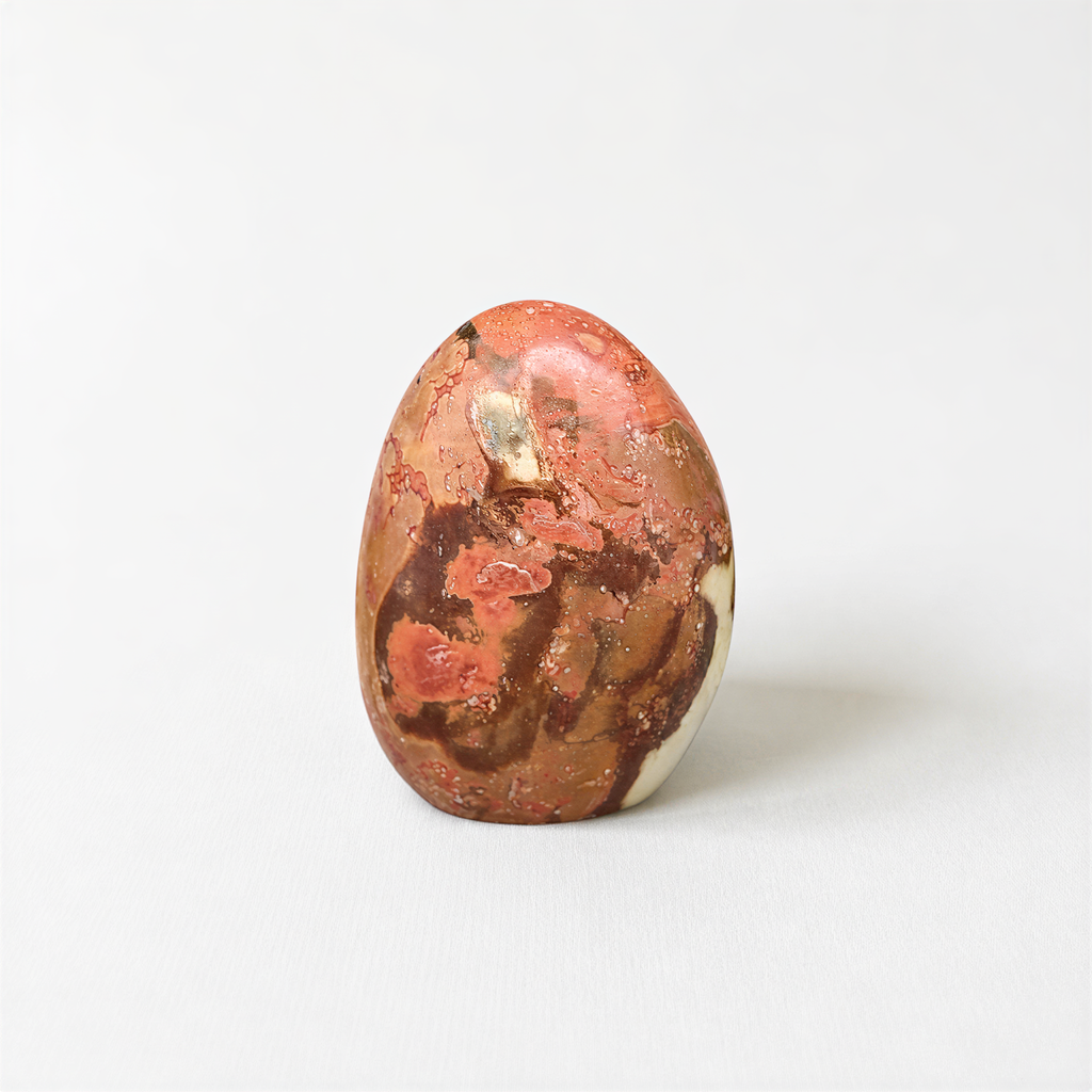 A single, round, orange-colored stone with a speckled surface sits on a plain white background.