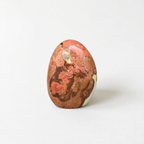 A single, round, orange-colored stone with a speckled surface sits on a plain white background.
