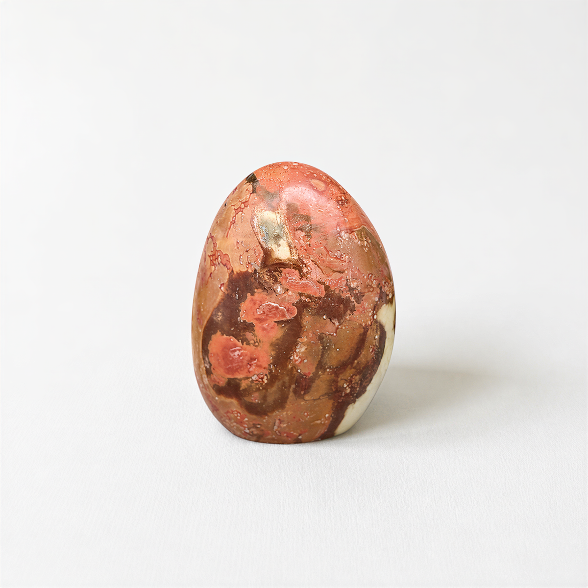 A single, round, orange-colored stone with a speckled surface sits on a plain white background.