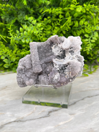 a piece of purple crystal or rock on a clear glass stand, placed on a marble surface.