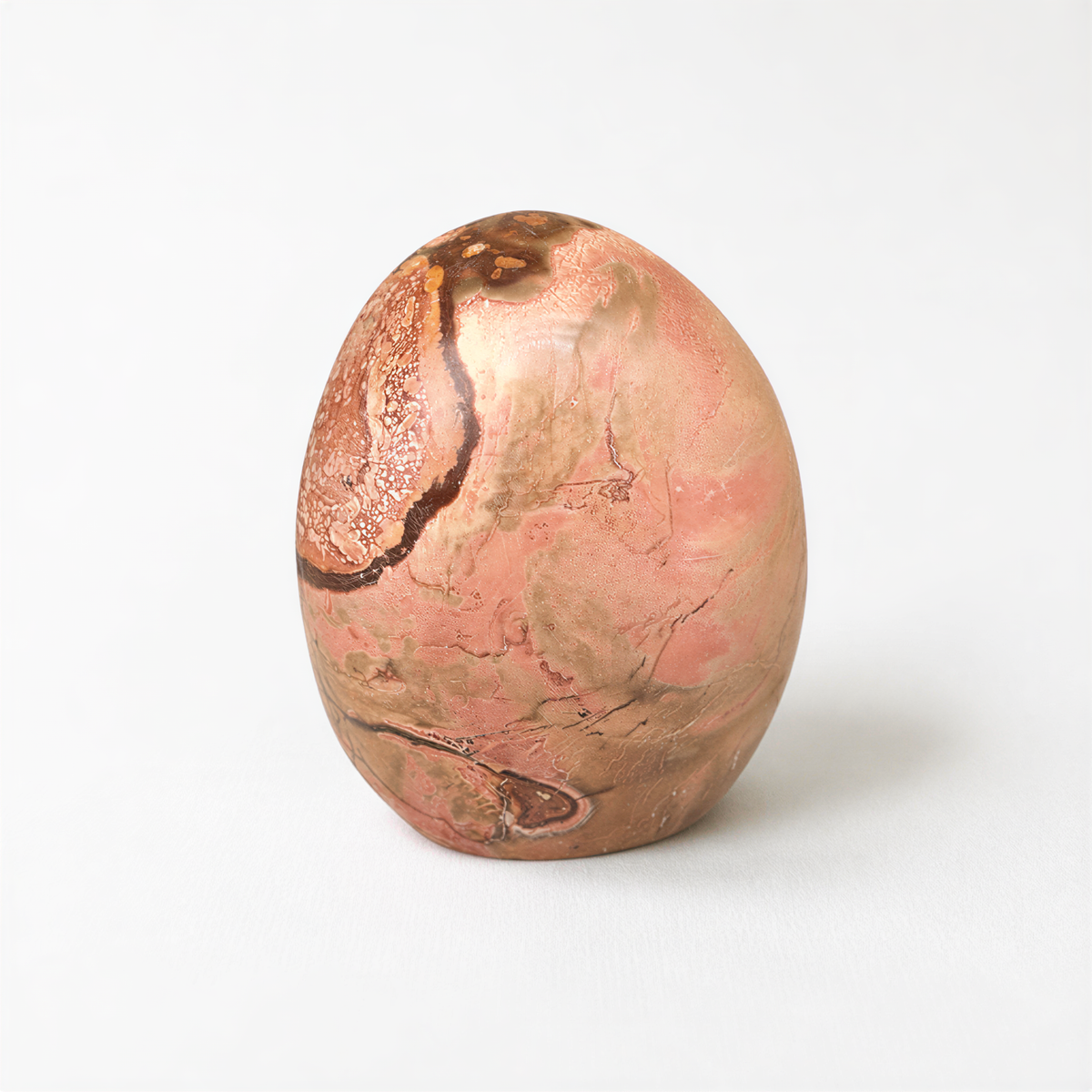 A round, textured stone or rock with a pinkish-brown hue, featuring a pattern of swirls and lines.