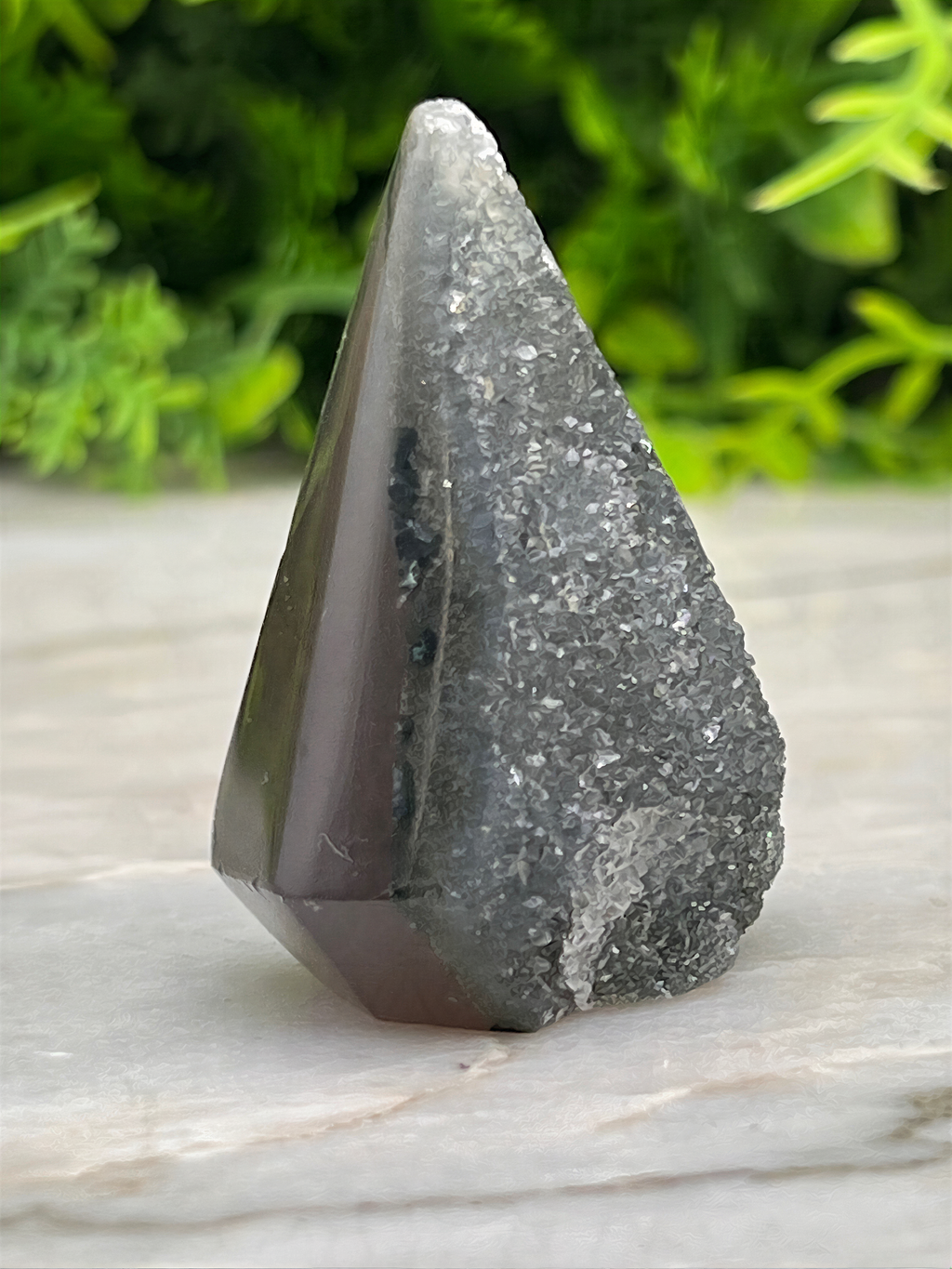 A close-up image of a dark gray, speckled rock with a pointed top, set against a blurred green background.