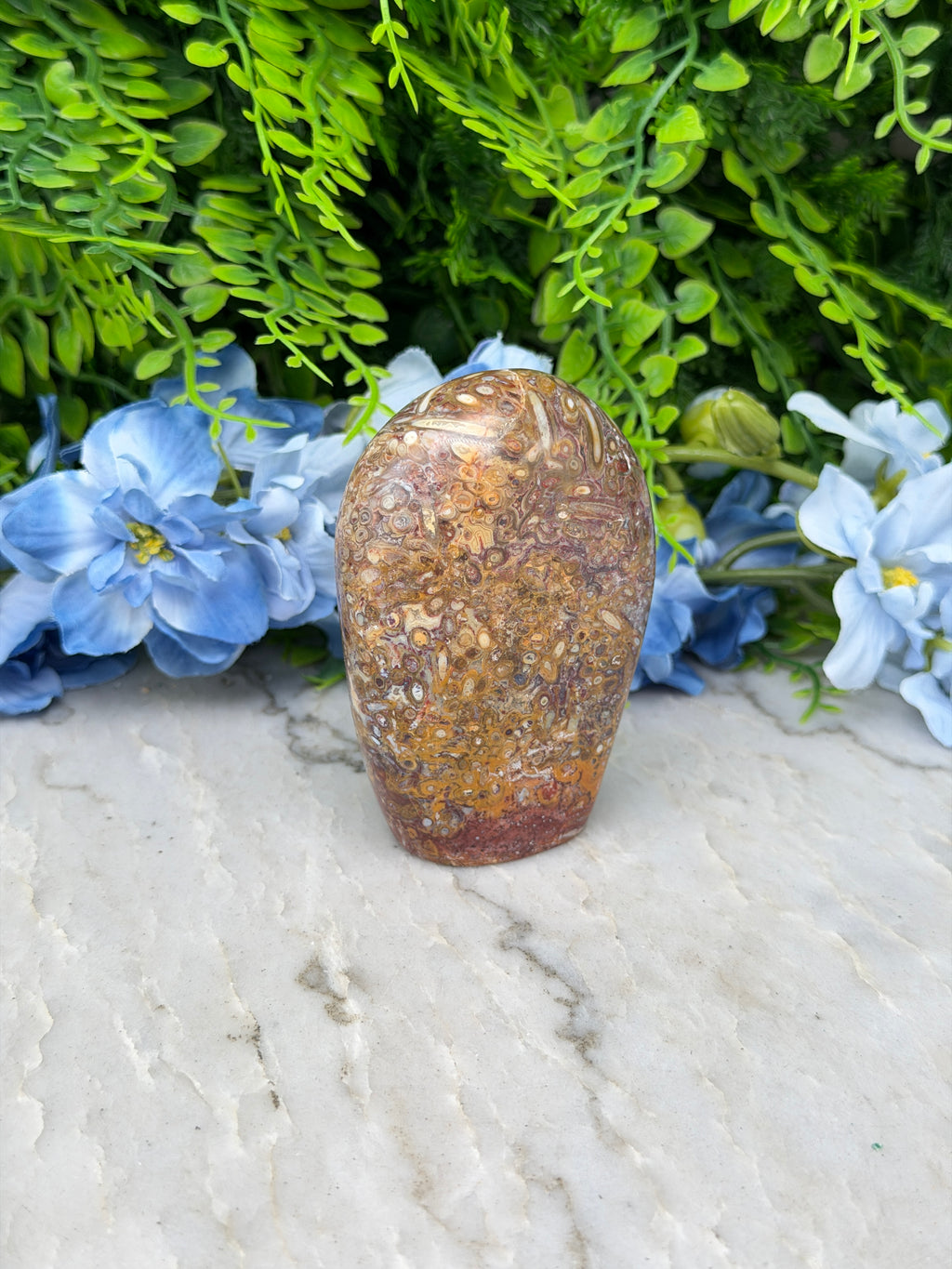 a close-up view of a rock with a brown and orange hue, surrounded by lush green foliage and delicate blue flowers.