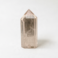 A single, clear crystal with a pointed top sits on a white surface.