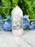 A white and green crystal sits on a marble surface, surrounded by blue flowers.
