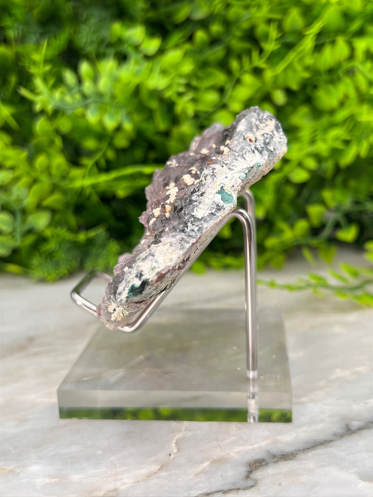 A piece of rock with a unique, irregular shape and a mix of gray and green colors, displayed on a clear stand.