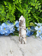 a marble-like stone or pendant resting on a bed of green foliage and blue flowers, creating a visually appealing contrast between the natural and man-made elements.