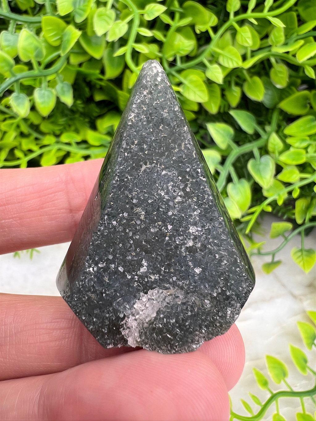 A hand is holding a triangular piece of black, speckled rock against a background of green foliage.