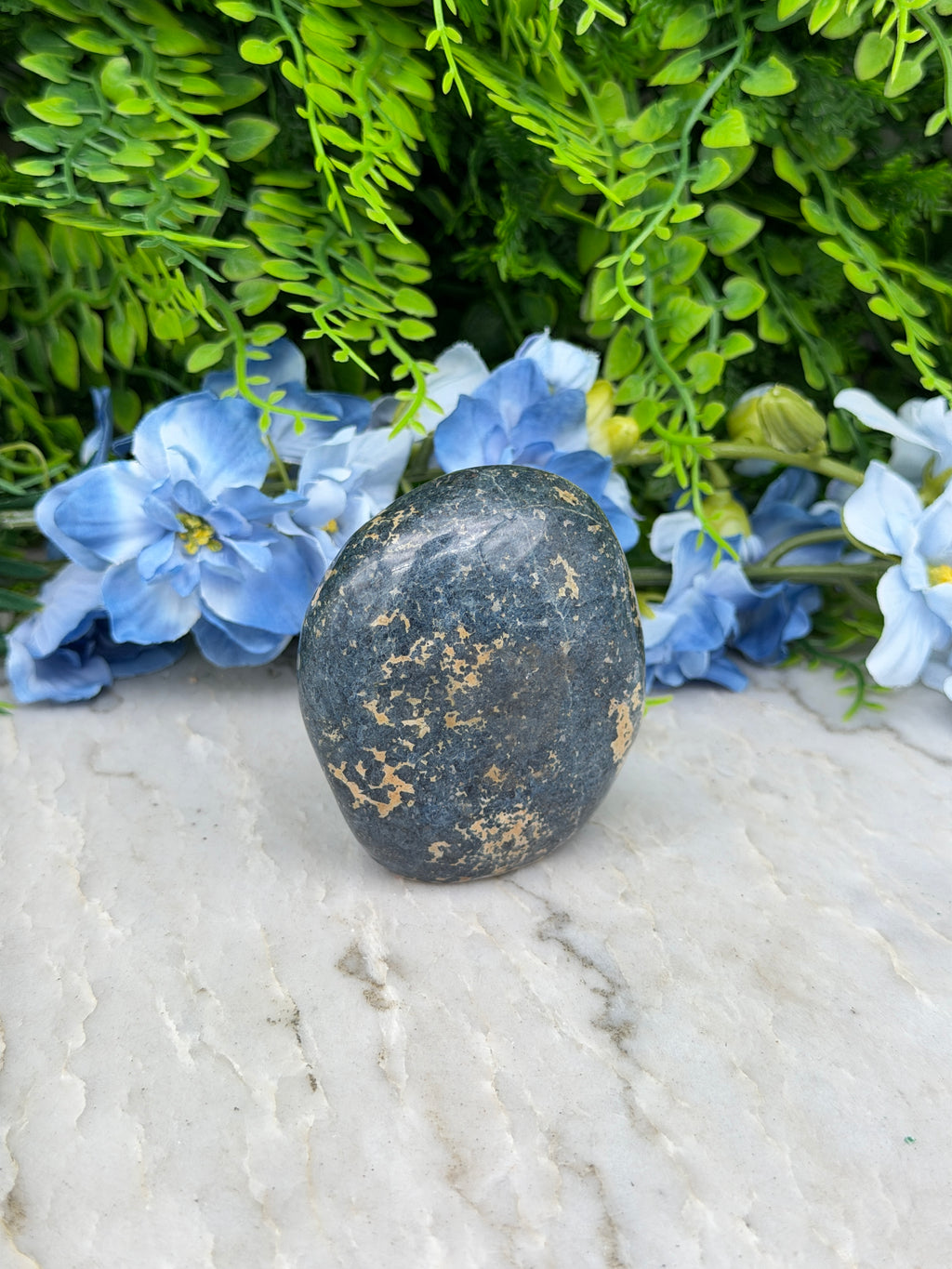 A black rock rests on a white surface, surrounded by vibrant blue flowers.