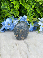 A black rock rests on a white surface, surrounded by vibrant blue flowers.