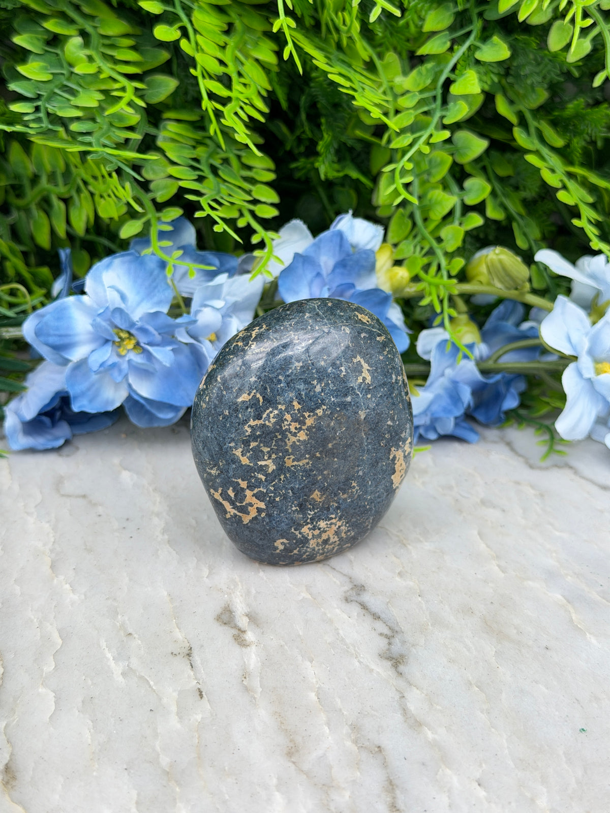 A black rock rests on a white surface, surrounded by vibrant blue flowers.